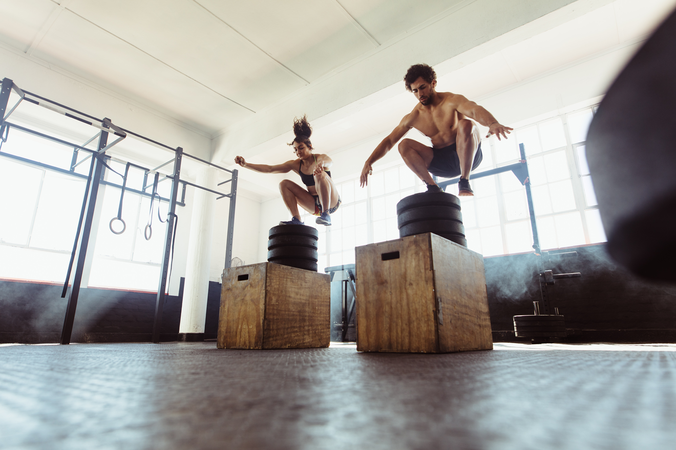 Man and woman jumping onto boxes at gym