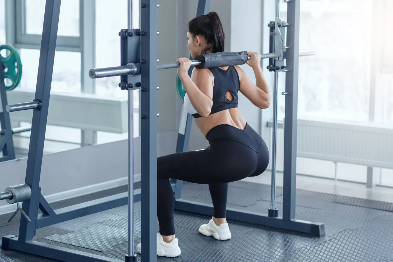 Woman doing Smith machine squat exercise in gym
