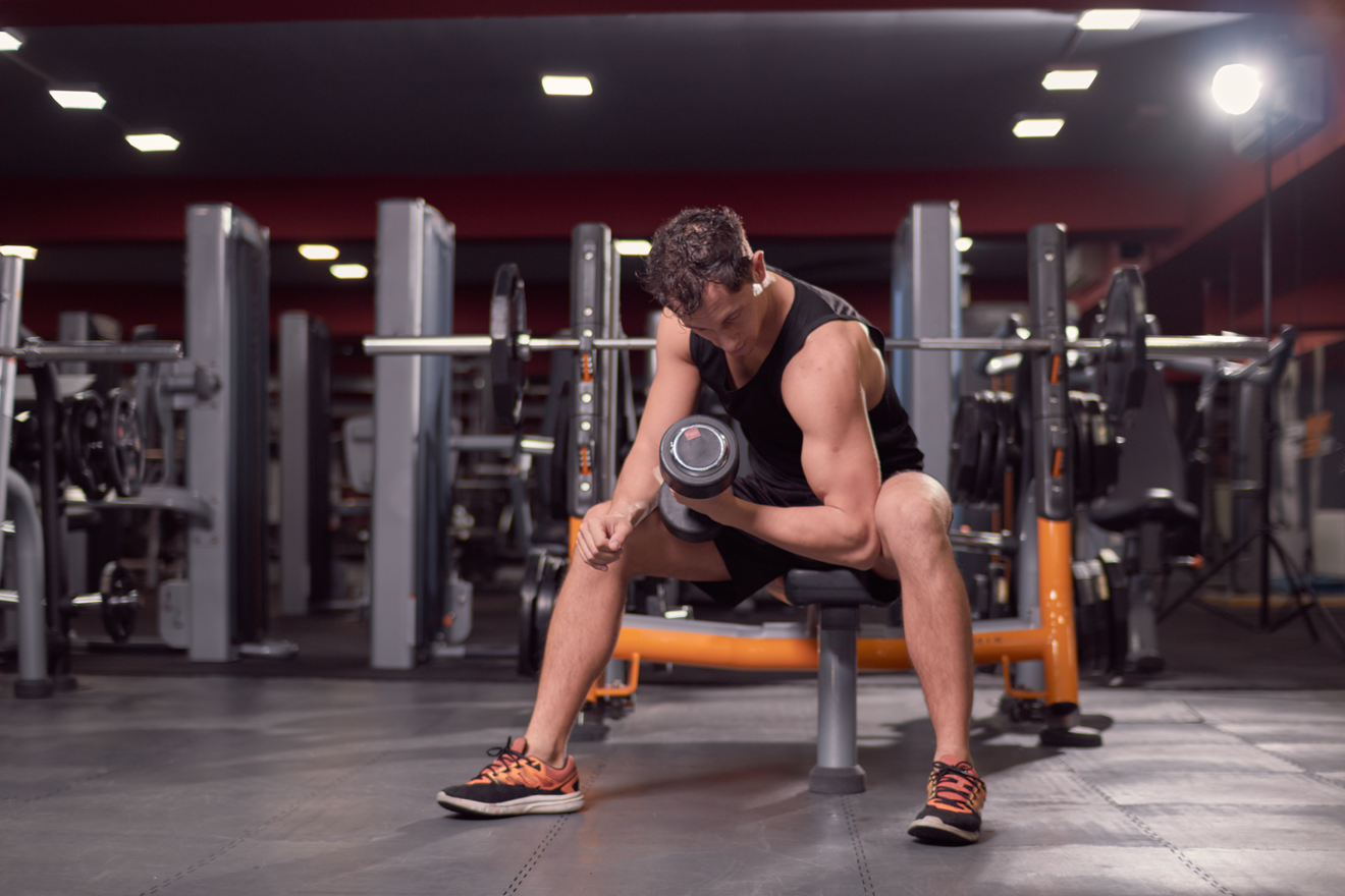Man sitting on bench doing dumbbell concentration curl