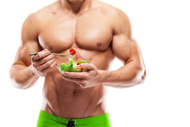 Topless muscular man eating a bowl of salad