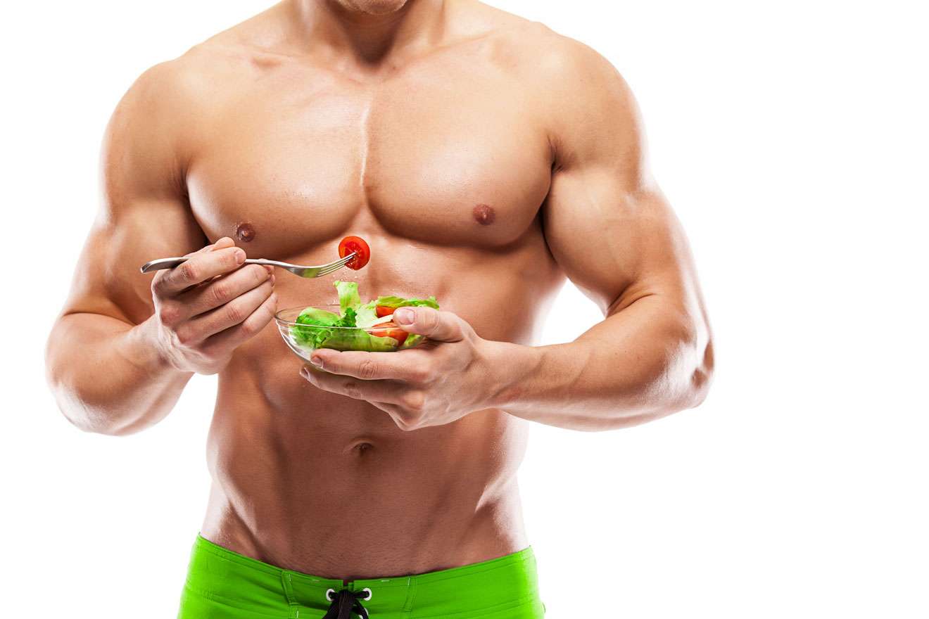 Topless muscular man eating a bowl of salad
