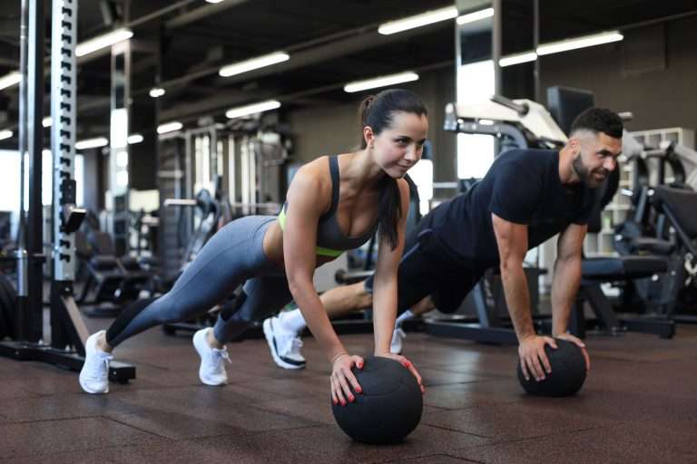 Fit man and woman in gym doing push-ups on medicine ball