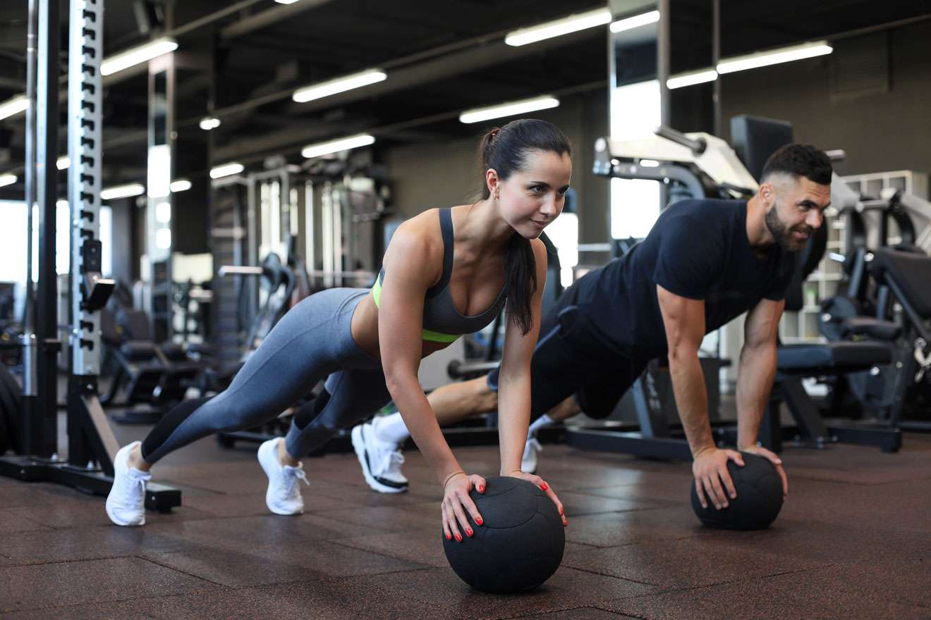 Fit man and woman in gym doing push-ups on medicine ball