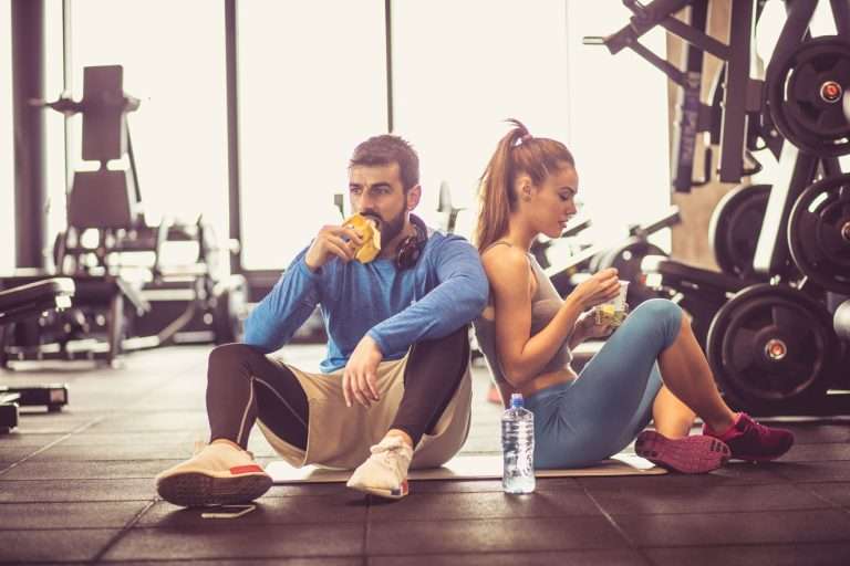 Young man and woman sitting and eating on gym floor